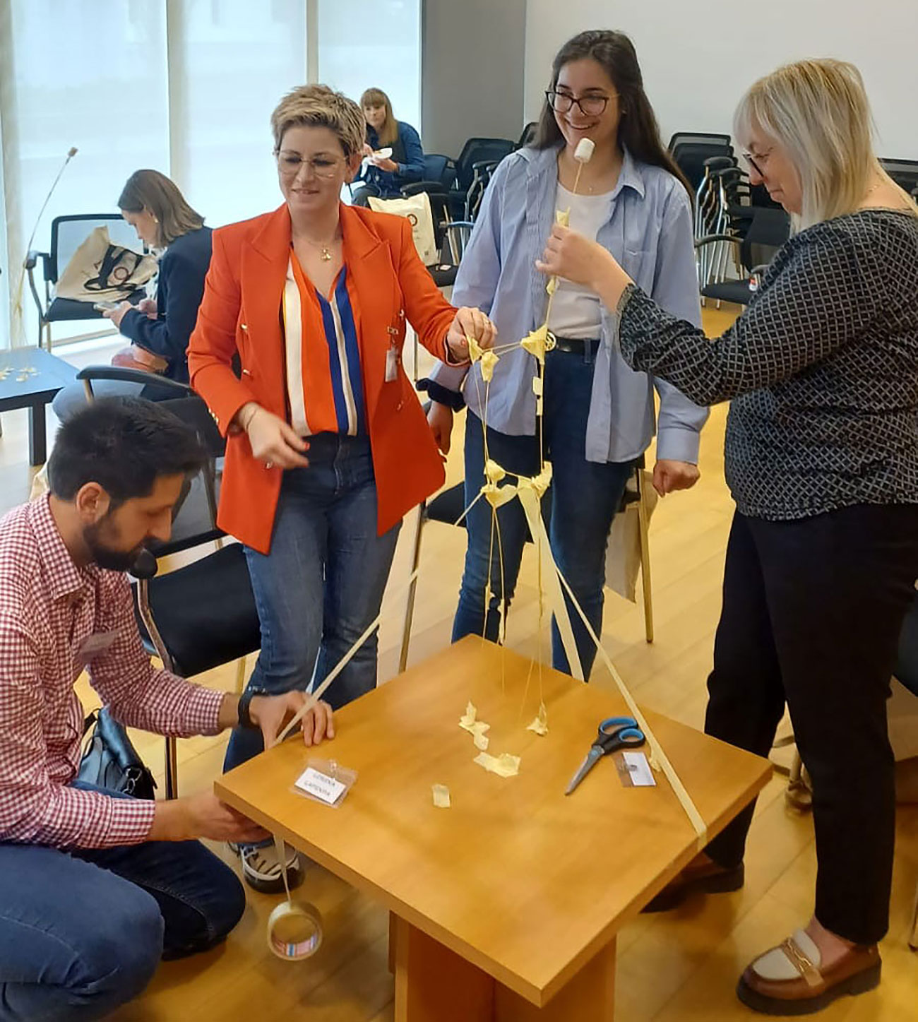 Sudionici radionice u manjim grupama grade toranj od tjestenine, samoljepljive trake i sljezovog kolačića kao primjer kako pristupiti procesu planiranja projekta.